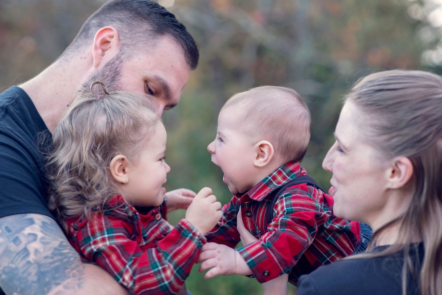 Happy family wearing matching red plaid clothing spending quality time together outdoors during a photo session.