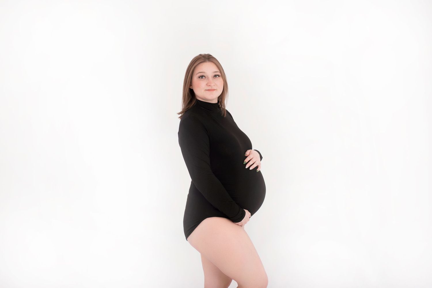 A pregnant figure in a black turtleneck bodysuit poses against a white background.