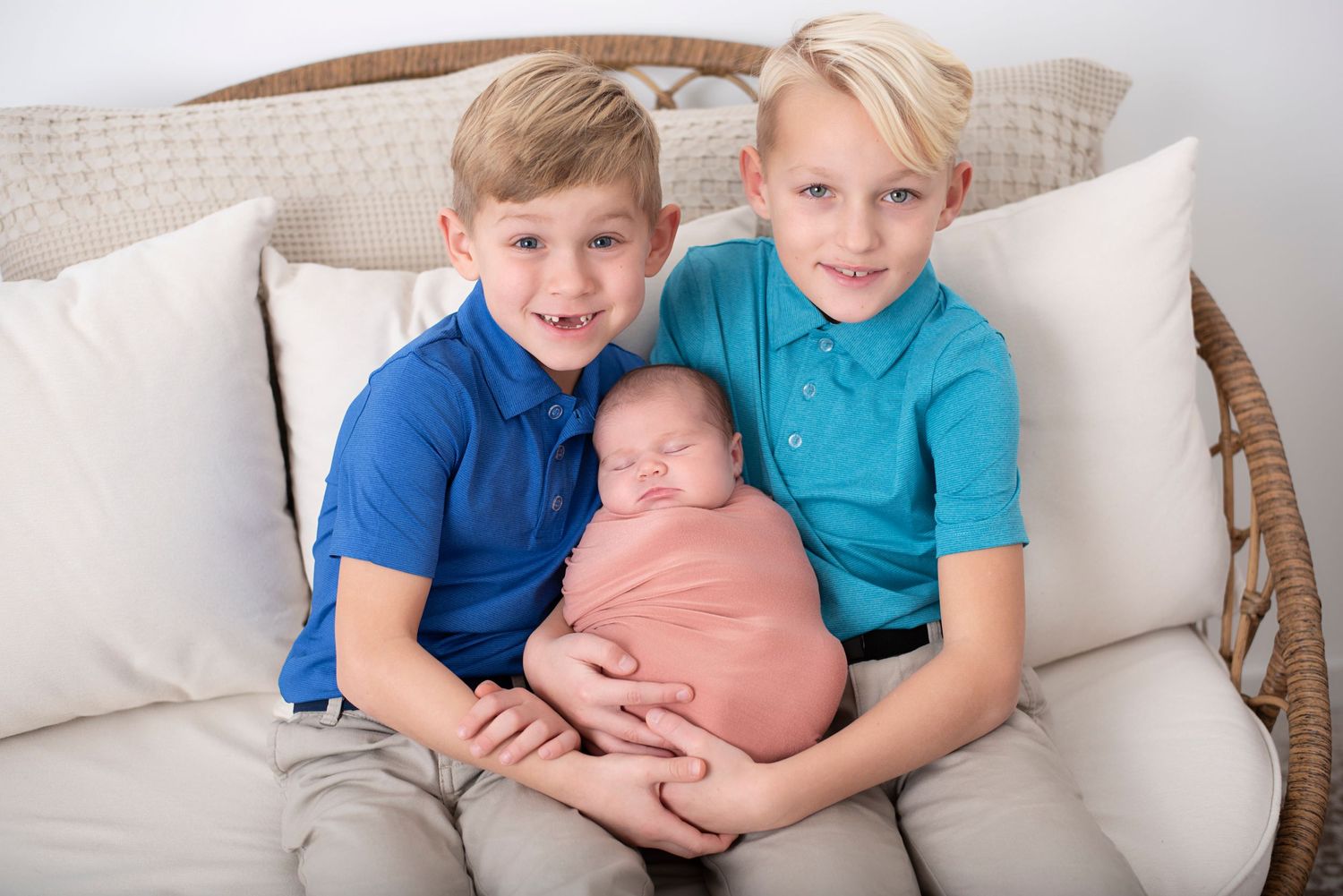 Three siblings sitting together on a beige couch against white pillows. Rhode Island Photographer