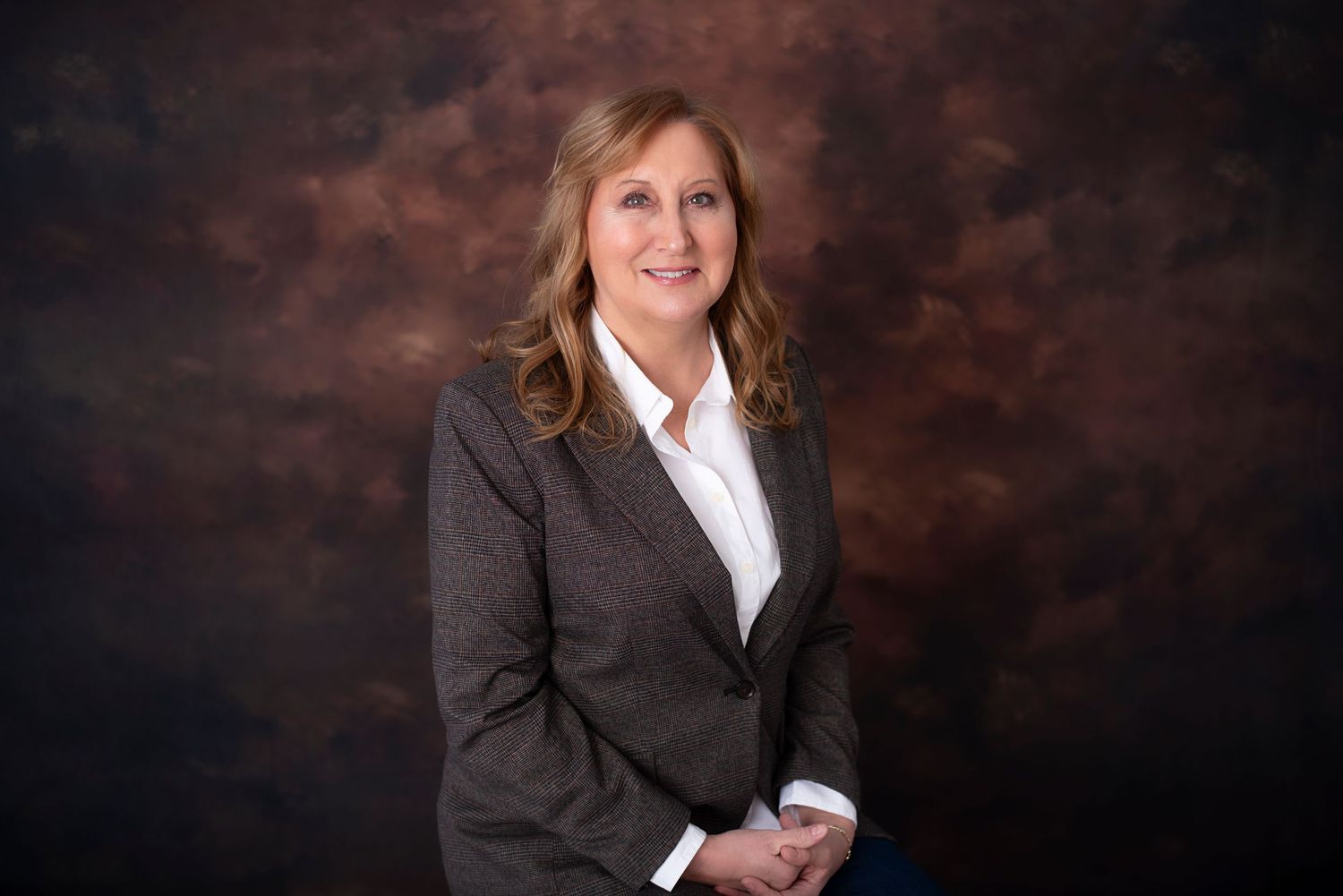 Professional headshot portrait against dark backdrop with person wearing business attire and warm smile.
