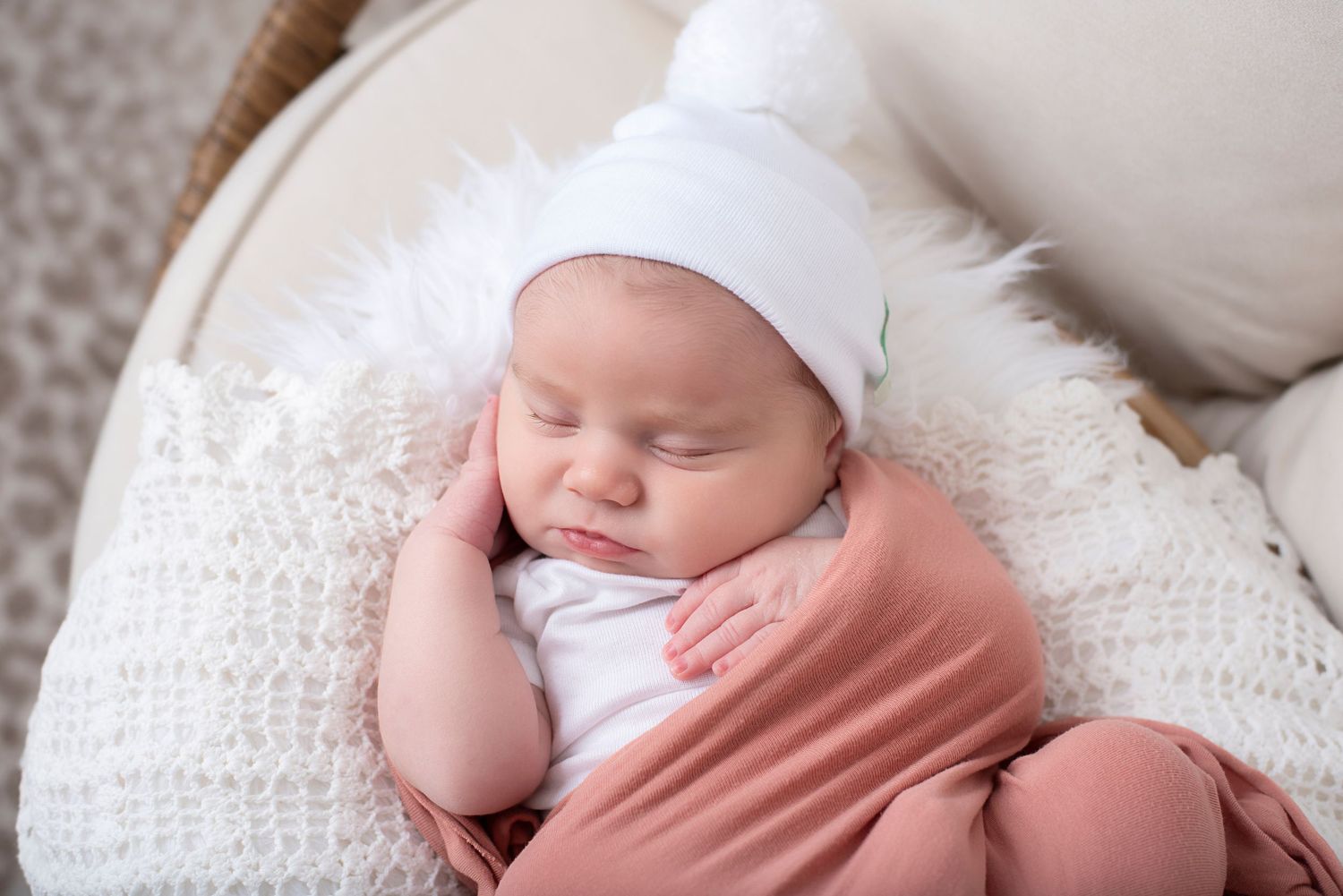 A newborn baby with white bonnet sleeping peacefully on soft white blankets in a series of gentle poses.