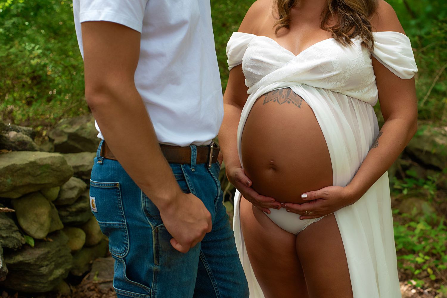 Intimate maternity portrait session showing white dress against rustic stone backdrop.