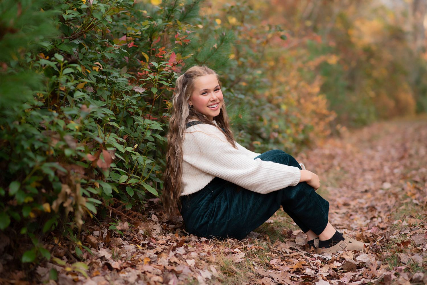 Person in white sweater sitting on autumn path with colorful fall foliage in background. Rhode Island Photographer