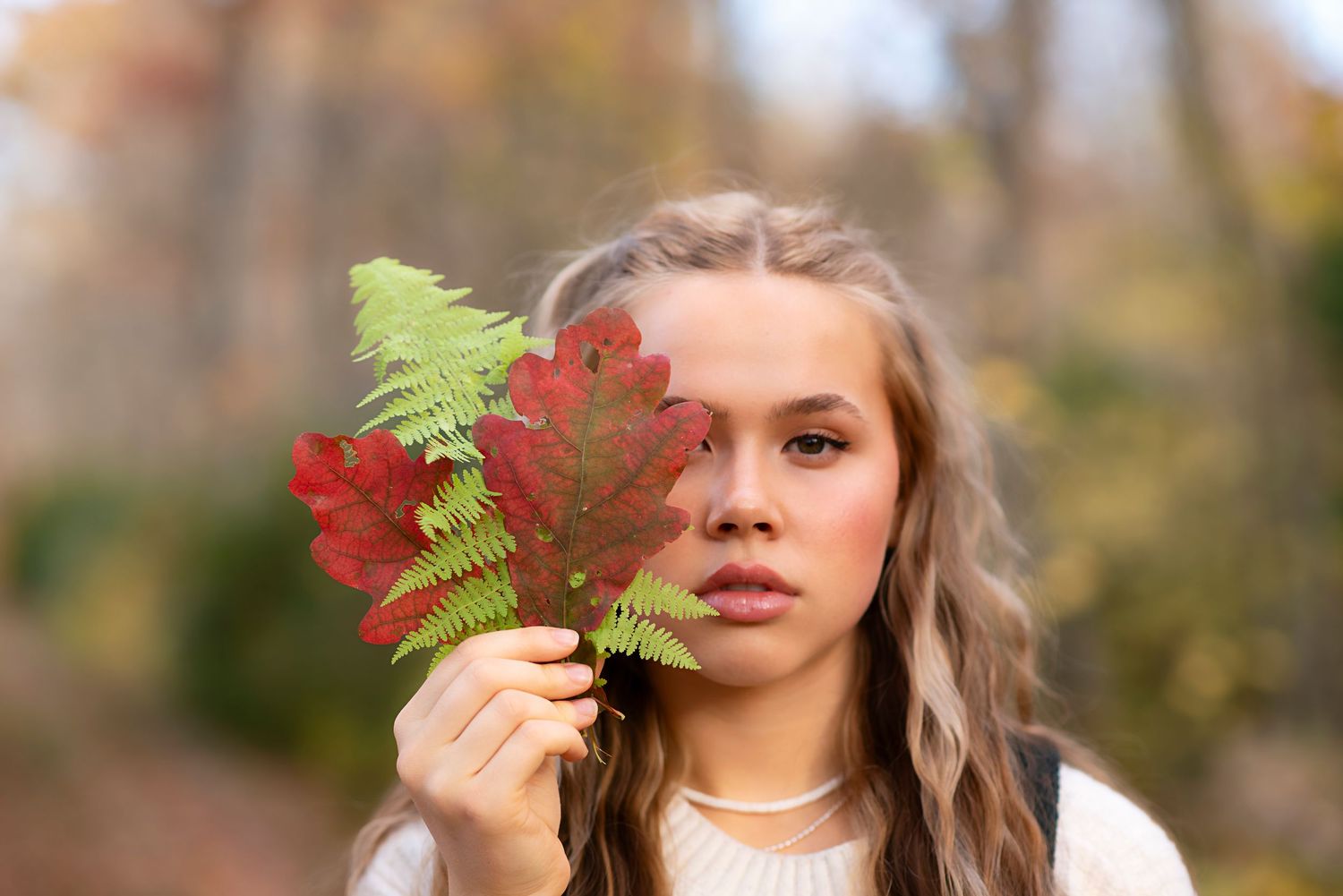 Collage of someone posing in autumn scenery holding various ferns and leaves against blurred natural background.