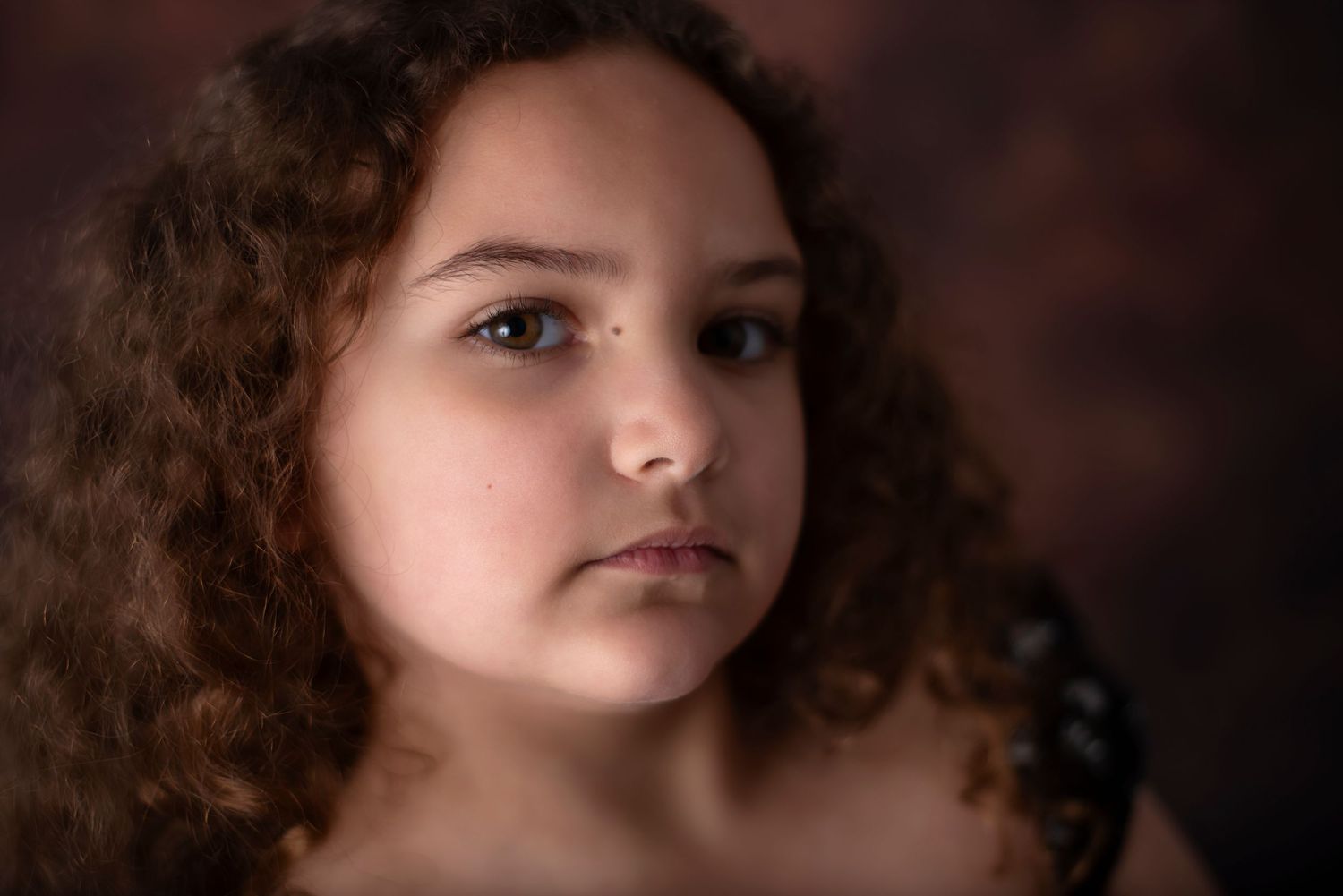 Portrait of someone with natural curly hair against a dark brown background with soft dramatic lighting.