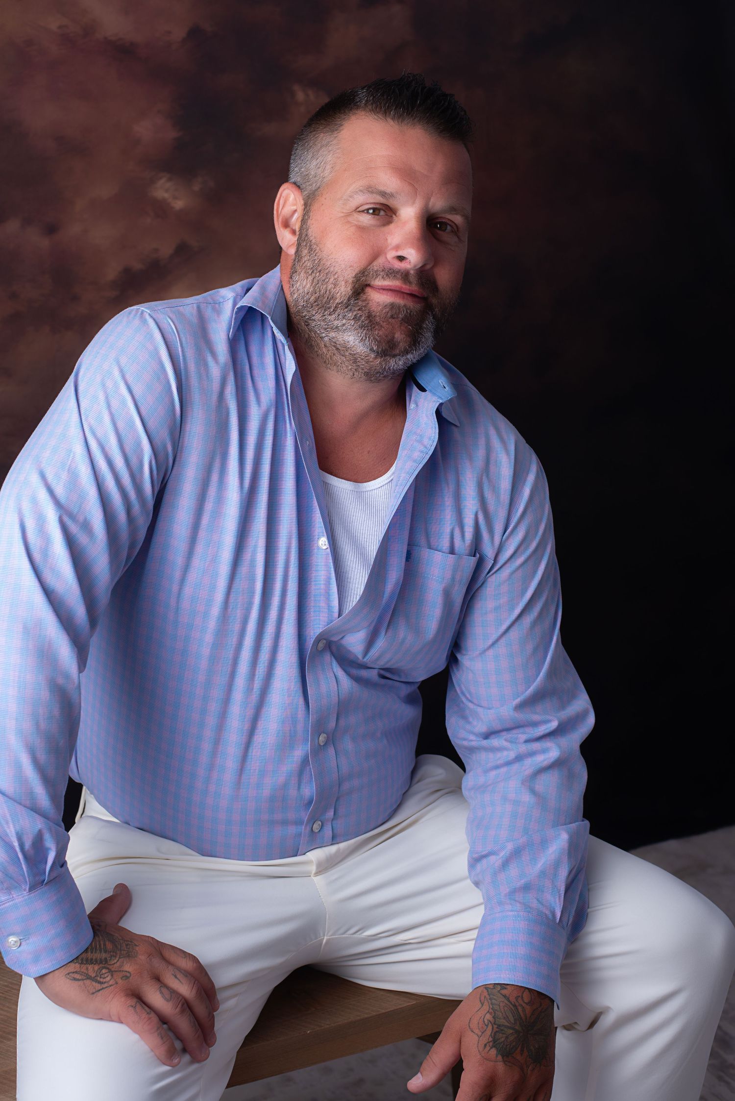 Professional portrait series showing someone in a light blue button-down shirt and white pants seated casually.