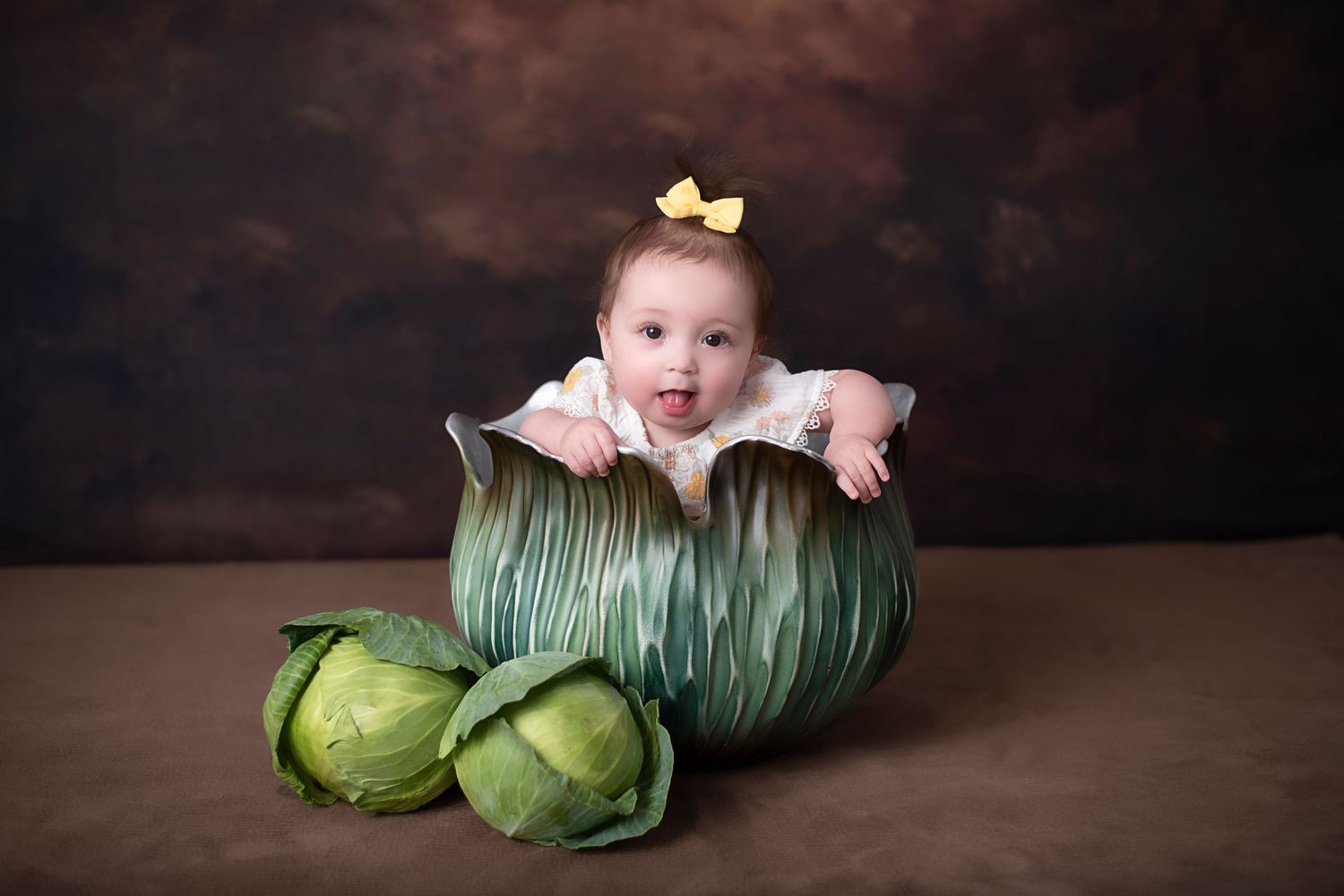 Creative baby portrait in a decorative green cabbage with artichokes setting against dark brown background.