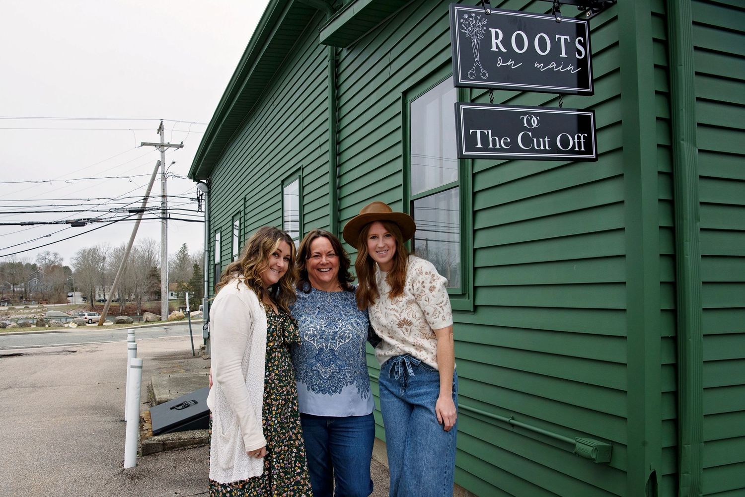 A group stands together outside a green building with a 'Roots' sign in a casual outdoor setting.