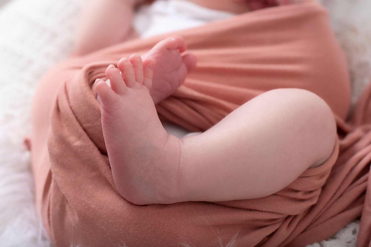 A closeup of tiny baby toes curled up in soft pink blankets shows tender newborn details.