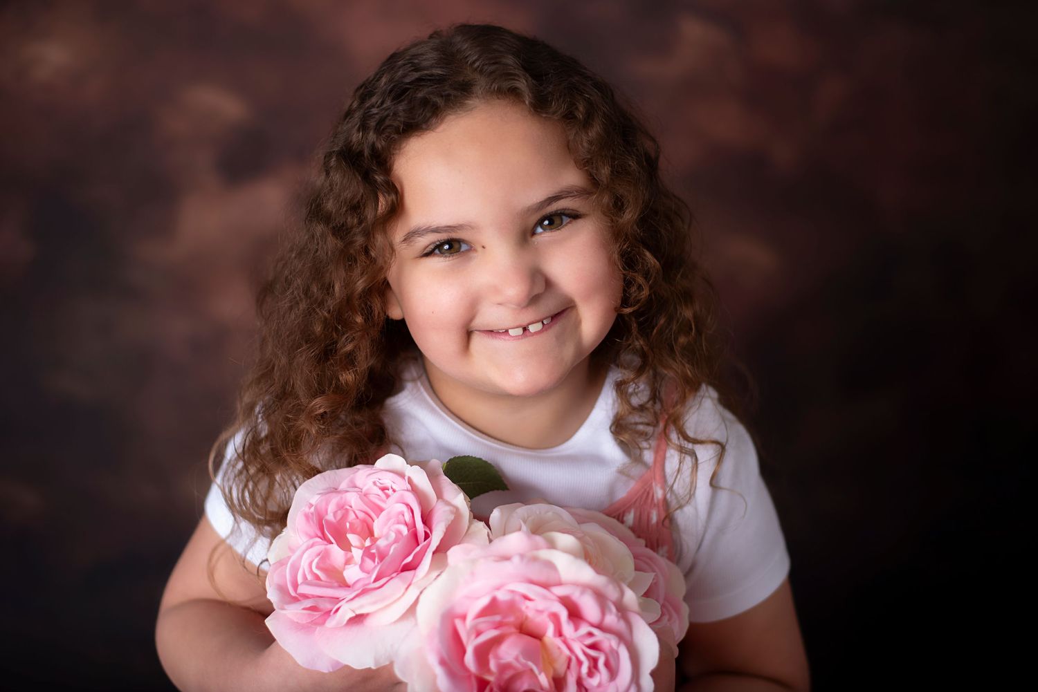 Professional studio portrait montage showing a child with curly hair holding pink roses against a dark brown backdrop.