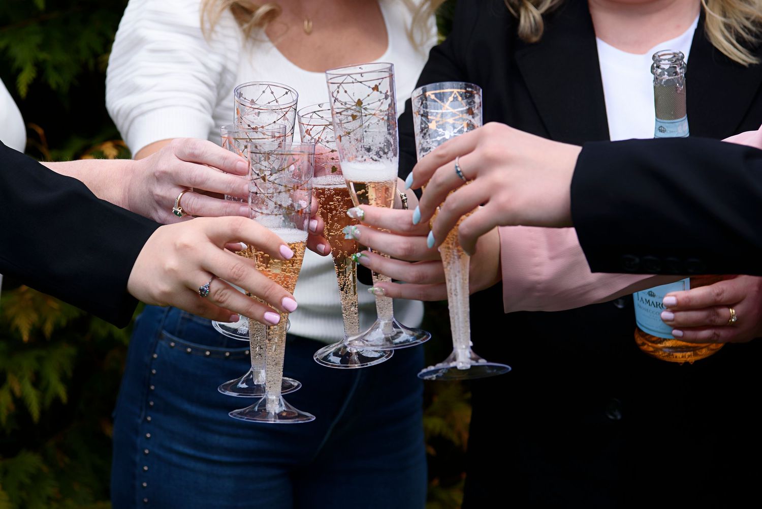 People holding champagne flutes and glasses together in a celebratory toast outdoors.