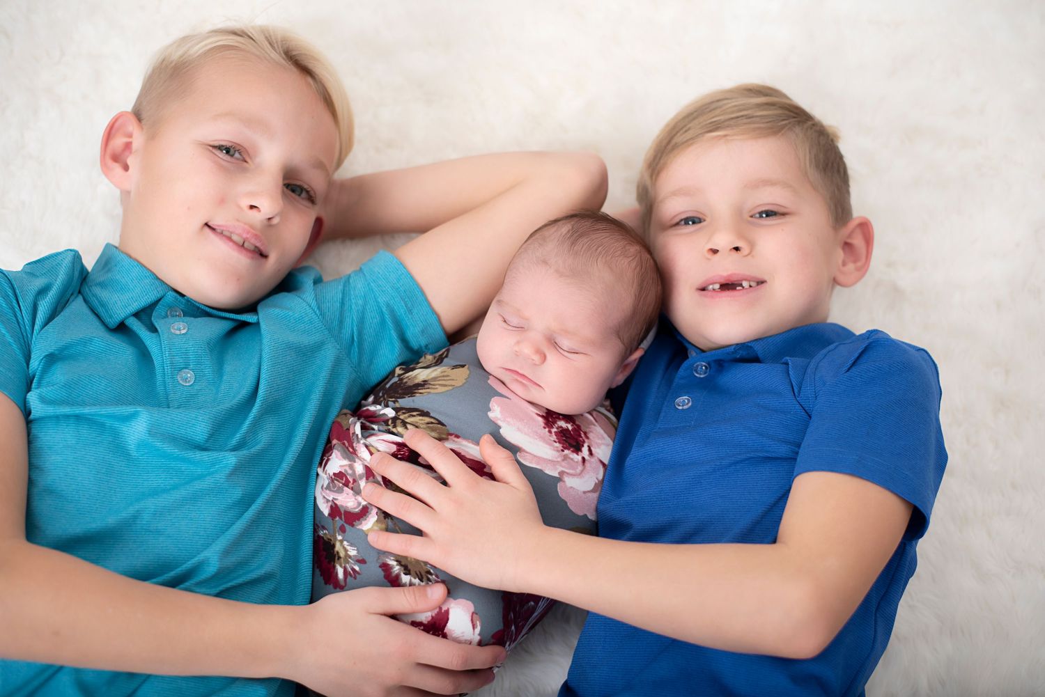 Three children laying together on a white background while smiling and embracing. Rhode Island Photographer