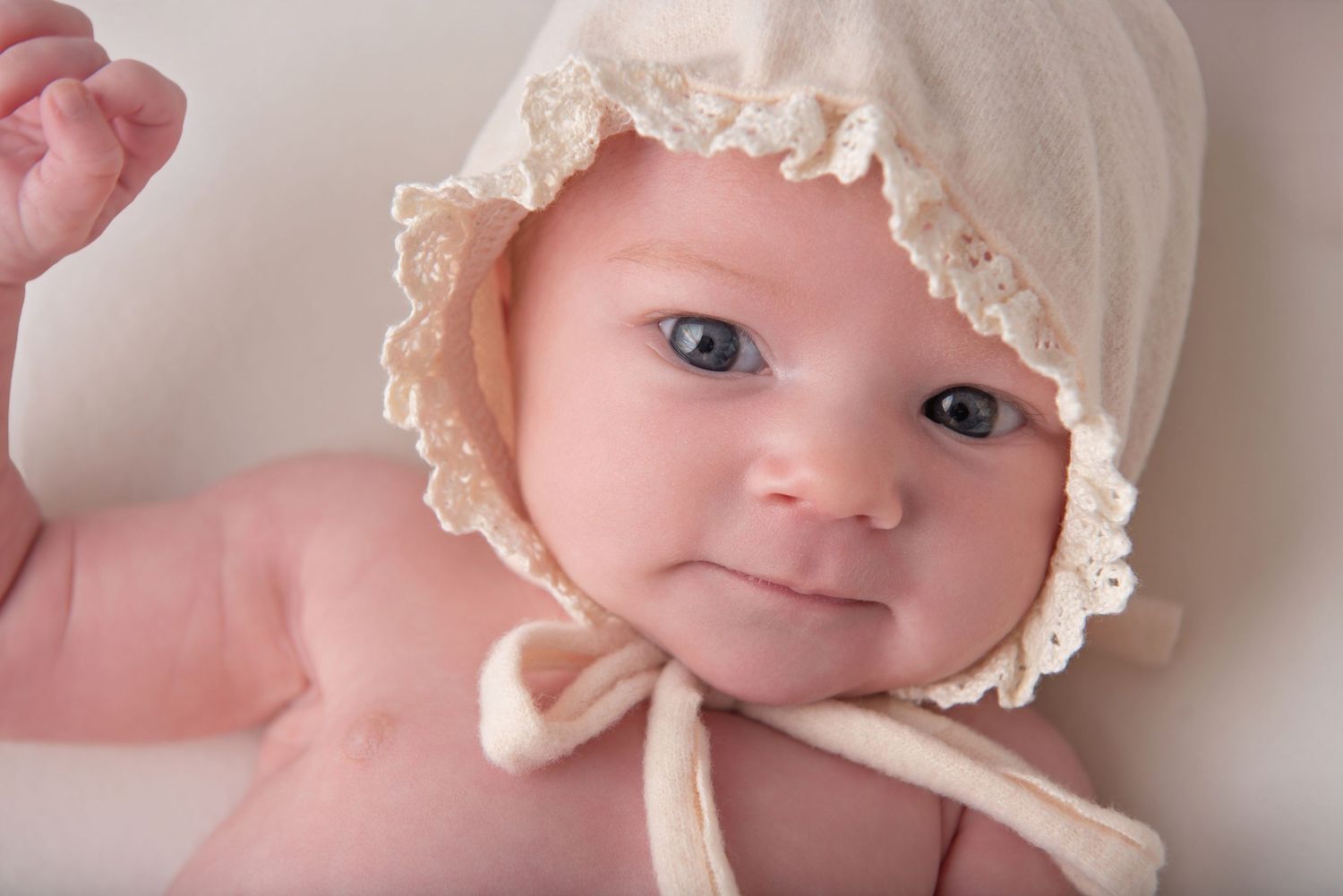 A baby wearing a cream-colored bonnet looks at the camera in a series of close-up shots. Rhode Island Newborn Photographer