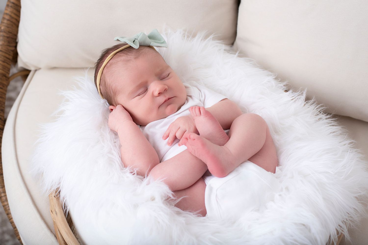 Sleeping newborn baby wearing pink wrap lying on soft white fur blanket in basket.