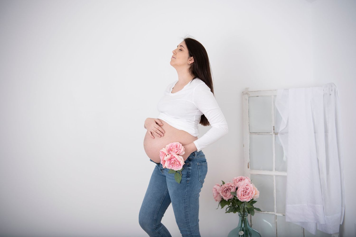 Person in jeans and white sweater moving gracefully in dance-like poses with pink roses in a bright studio.