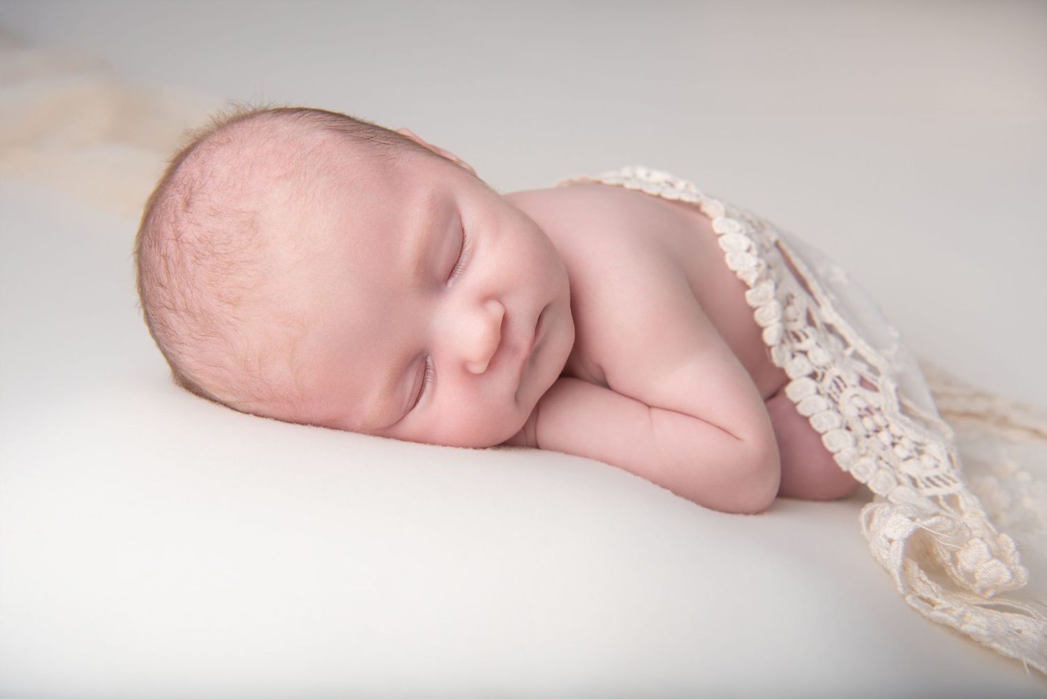 Peaceful newborn baby sleeping wrapped in delicate lace blanket on white background.