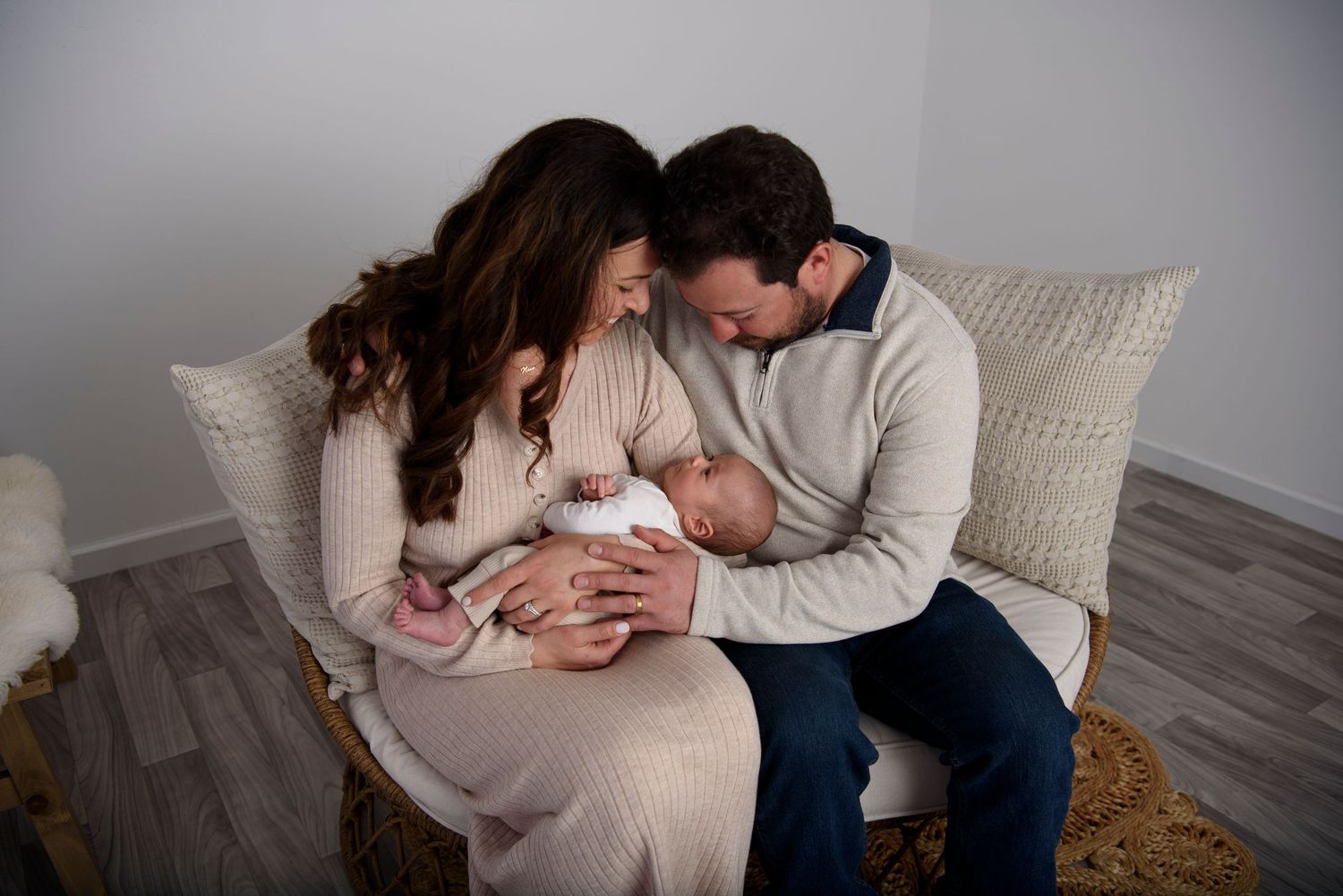 A loving couple in casual sweaters embraces tenderly while sitting on a cozy gray couch at home.