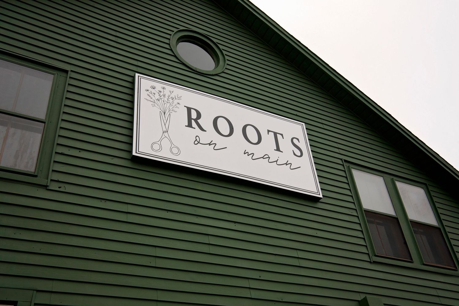 A white business sign reading 'ROOTS' mounted on a dark green building exterior.