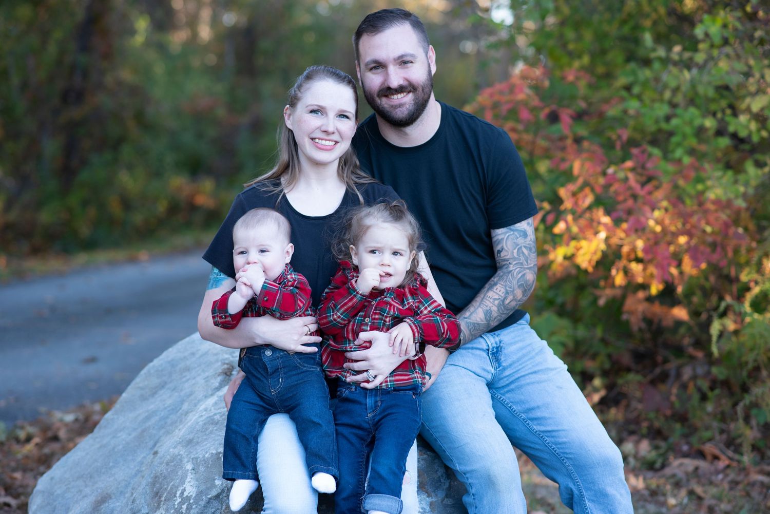 A family sits together on a large rock along an autumn path with colorful fall foliage in the background.