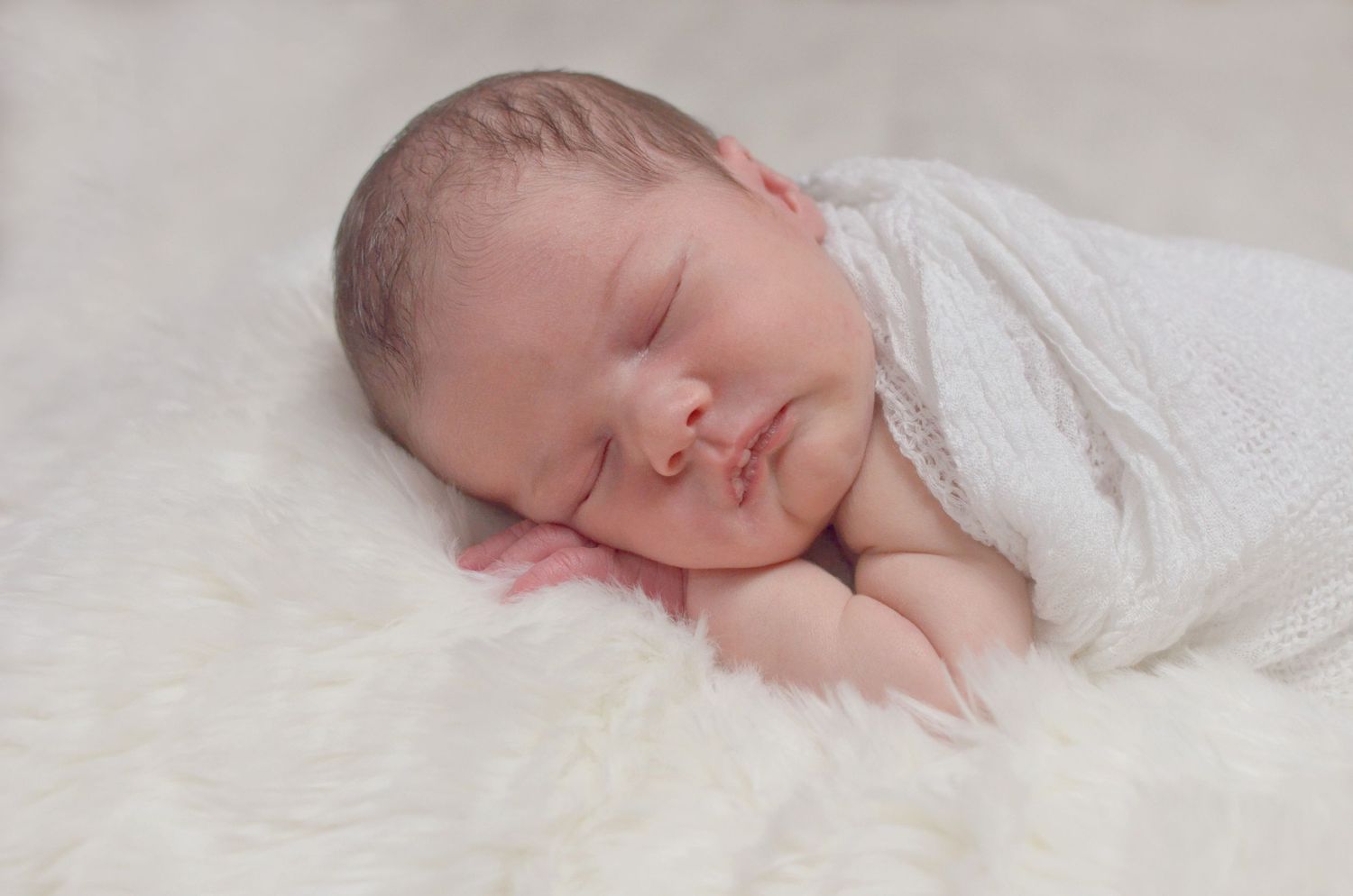 Newborn baby sleeping peacefully on soft white fabric in a series of gentle poses.