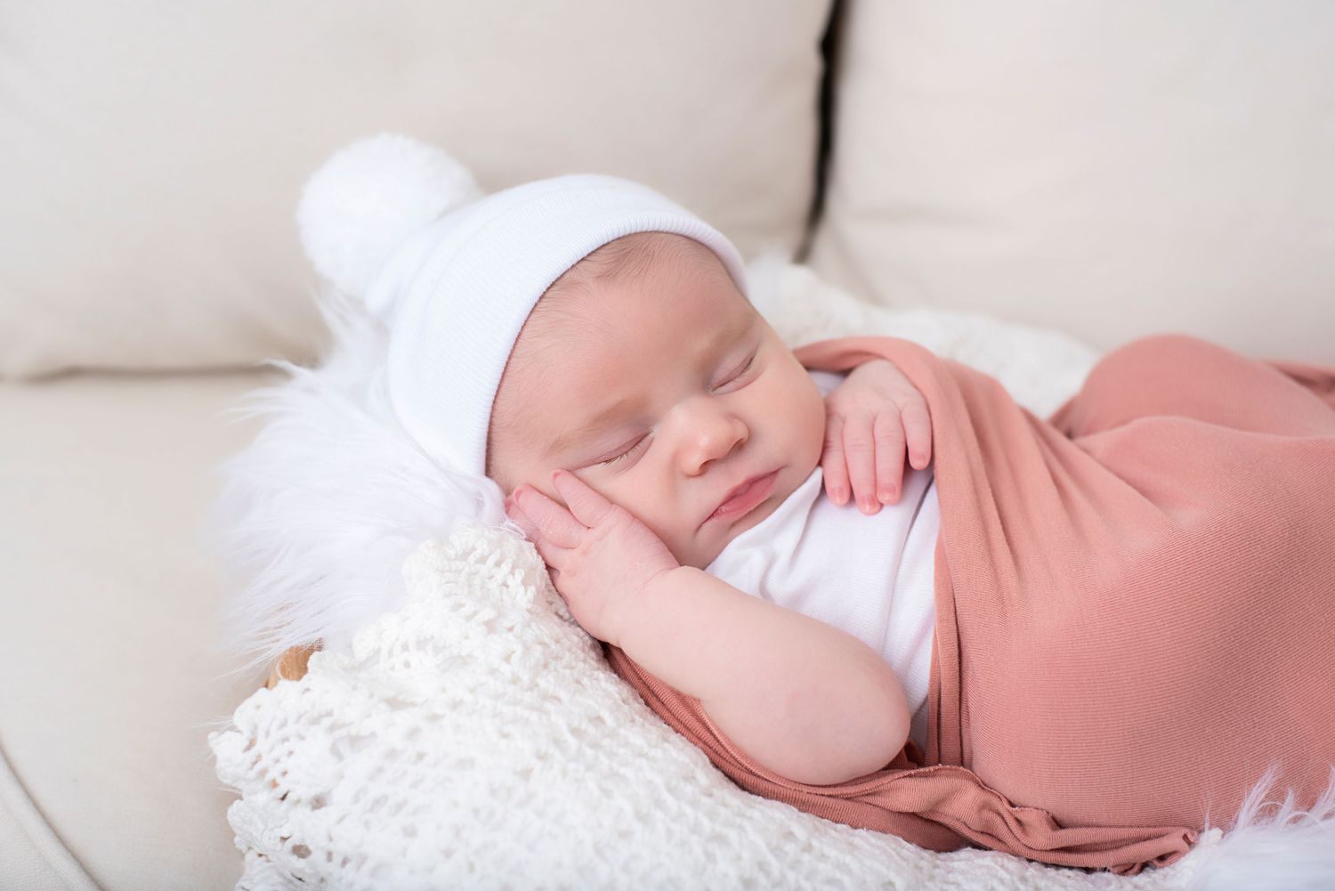 Sleeping newborn in pink swaddle blanket resting on white textured surface.
