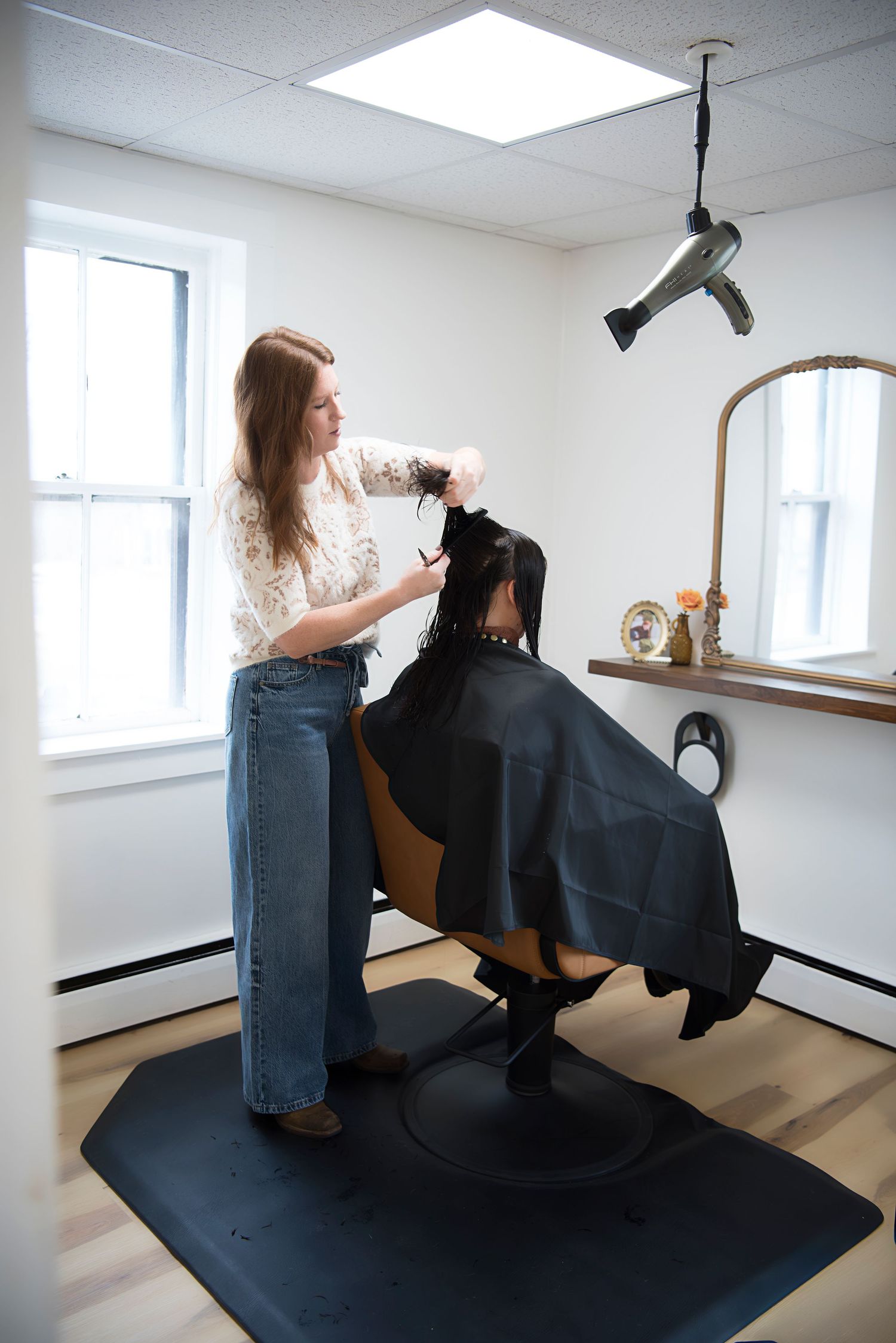 A sequence of photos shows a hairstylist cutting a client's hair in a minimalist white studio space with black floor mat.