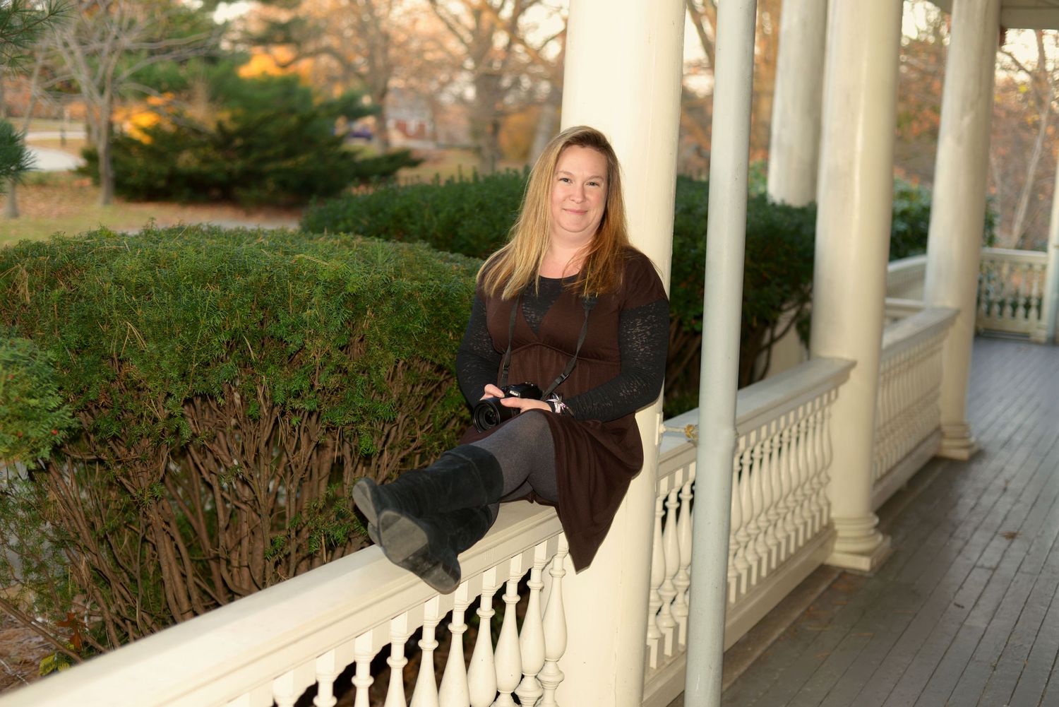 A person sits on a white porch railing with autumn foliage in the background at Roger Williams Park .