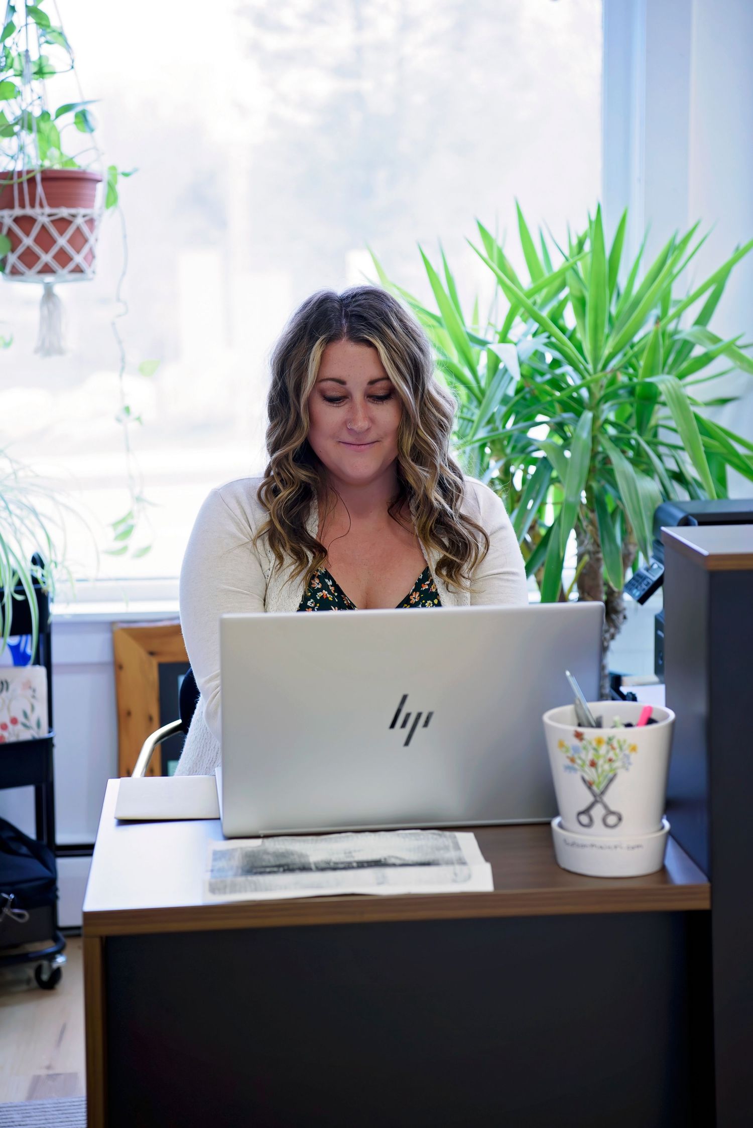 A bright workspace with plants and natural light featuring an HP laptop on a wooden desk.