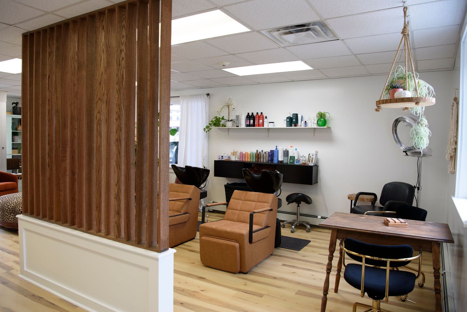 Modern salon interior with wood accent wall, tan leather chairs, and floating shelves in a bright white room.