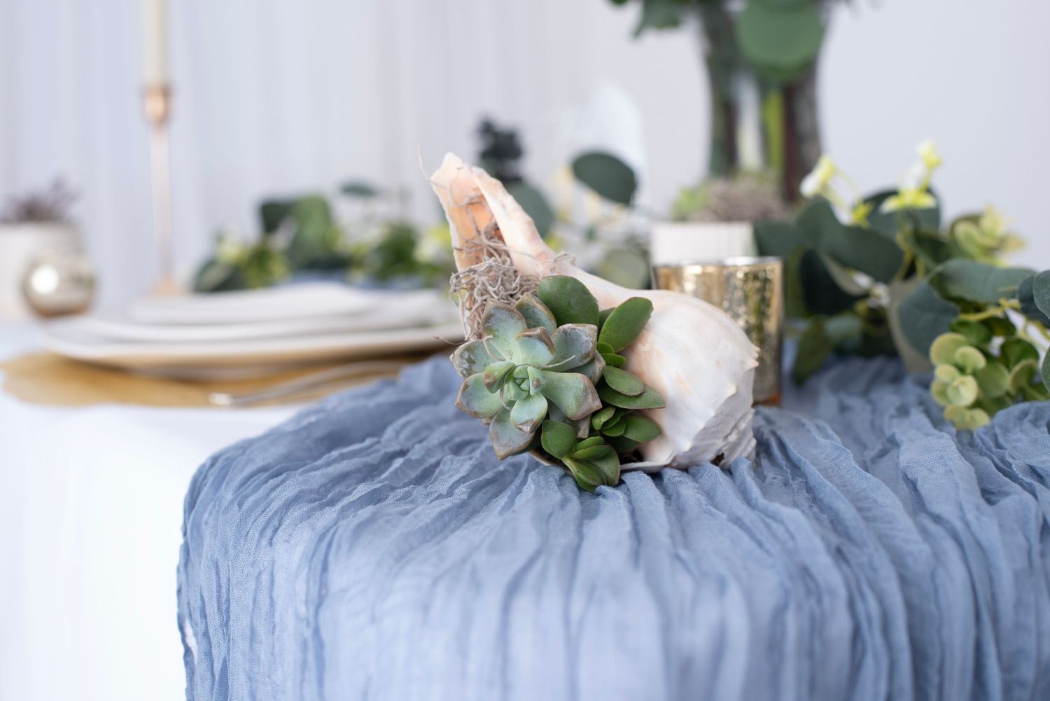 Close-up view of floral centerpiece with coral gerberas and eucalyptus on dusty blue table runner.