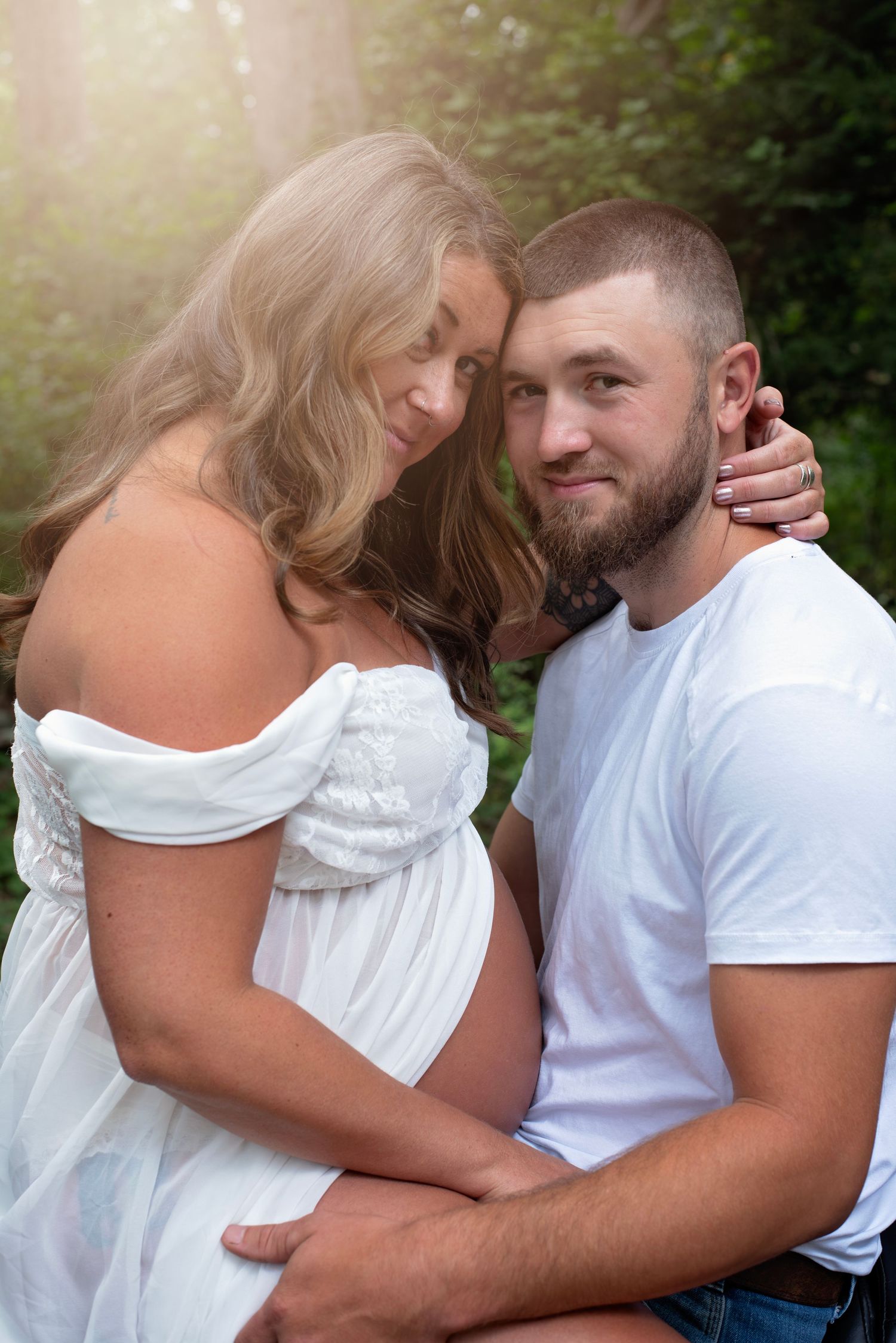 A couple in white embracing affectionately during an outdoor photoshoot with natural lighting.