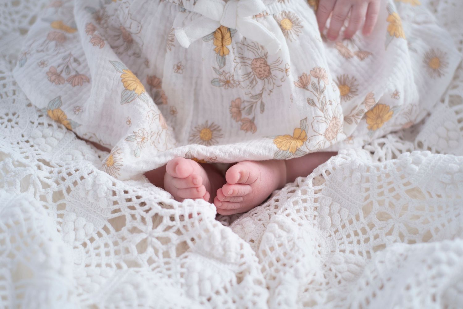 Tiny baby feet peek out from under delicate white lace blanket with floral patterns. Rhode Island Photographer