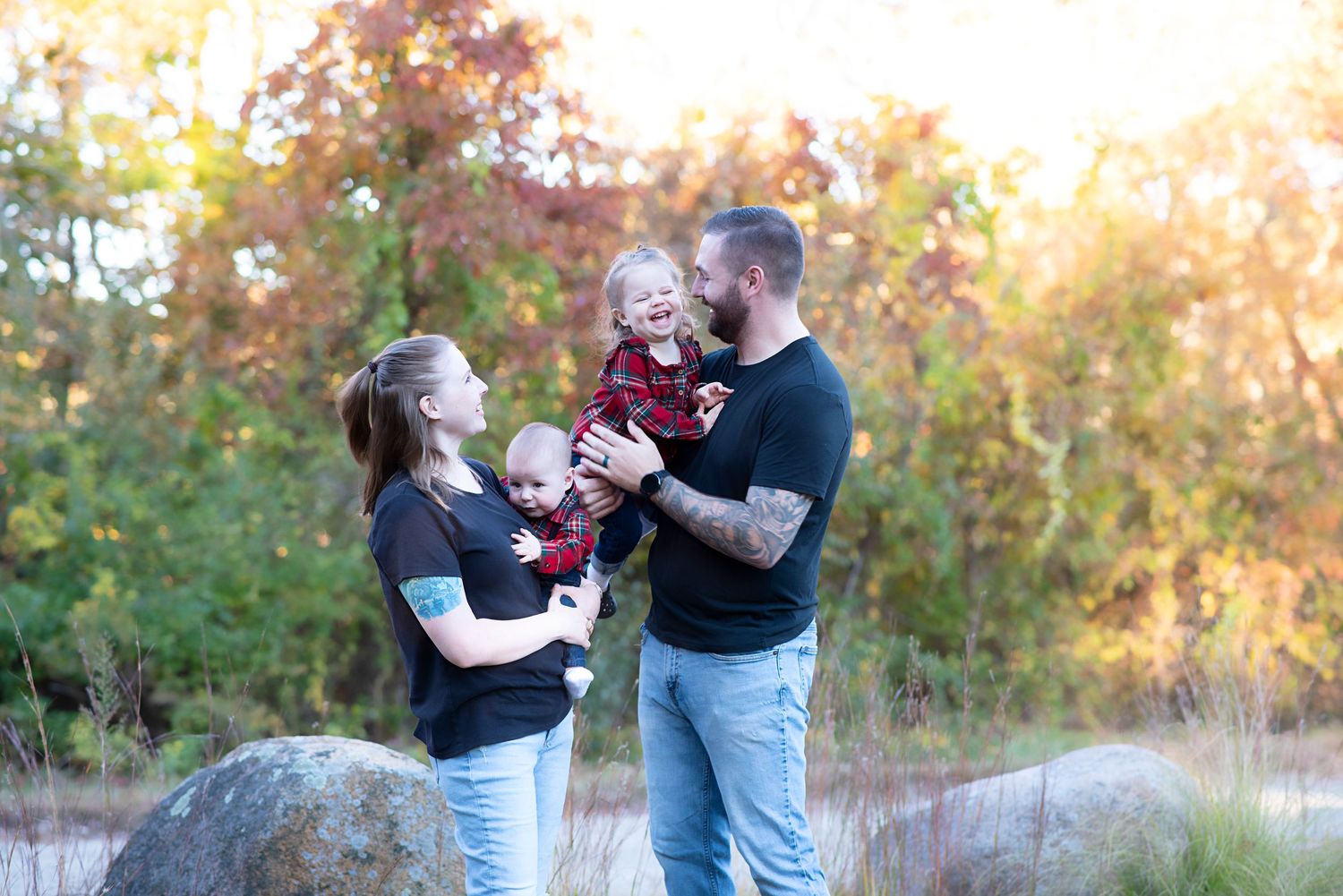 A family enjoys a tender moment together outdoors during golden hour with autumn foliage in the background.
