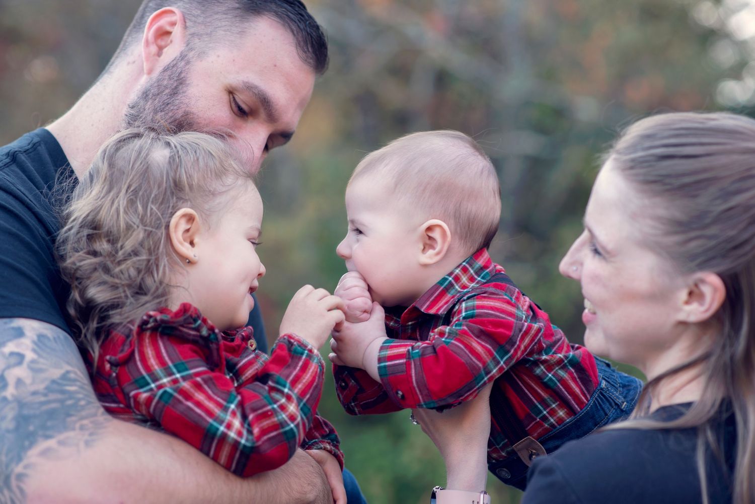 A family dressed in plaid clothing shares a tender outdoor moment together during a photo session.