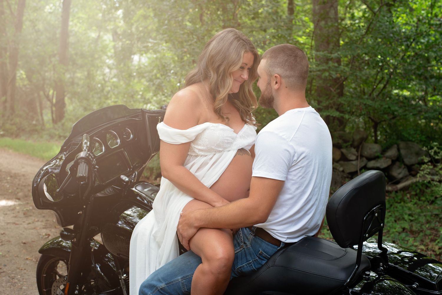 A couple sits intimately together along a sunny forest path during an outdoor photo session.