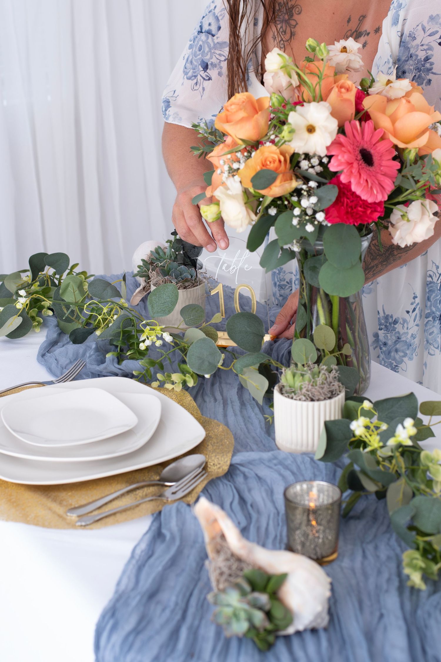 Elegant table setting with coral and white flowers, blue chiffon runner, and rustic wooden accents.