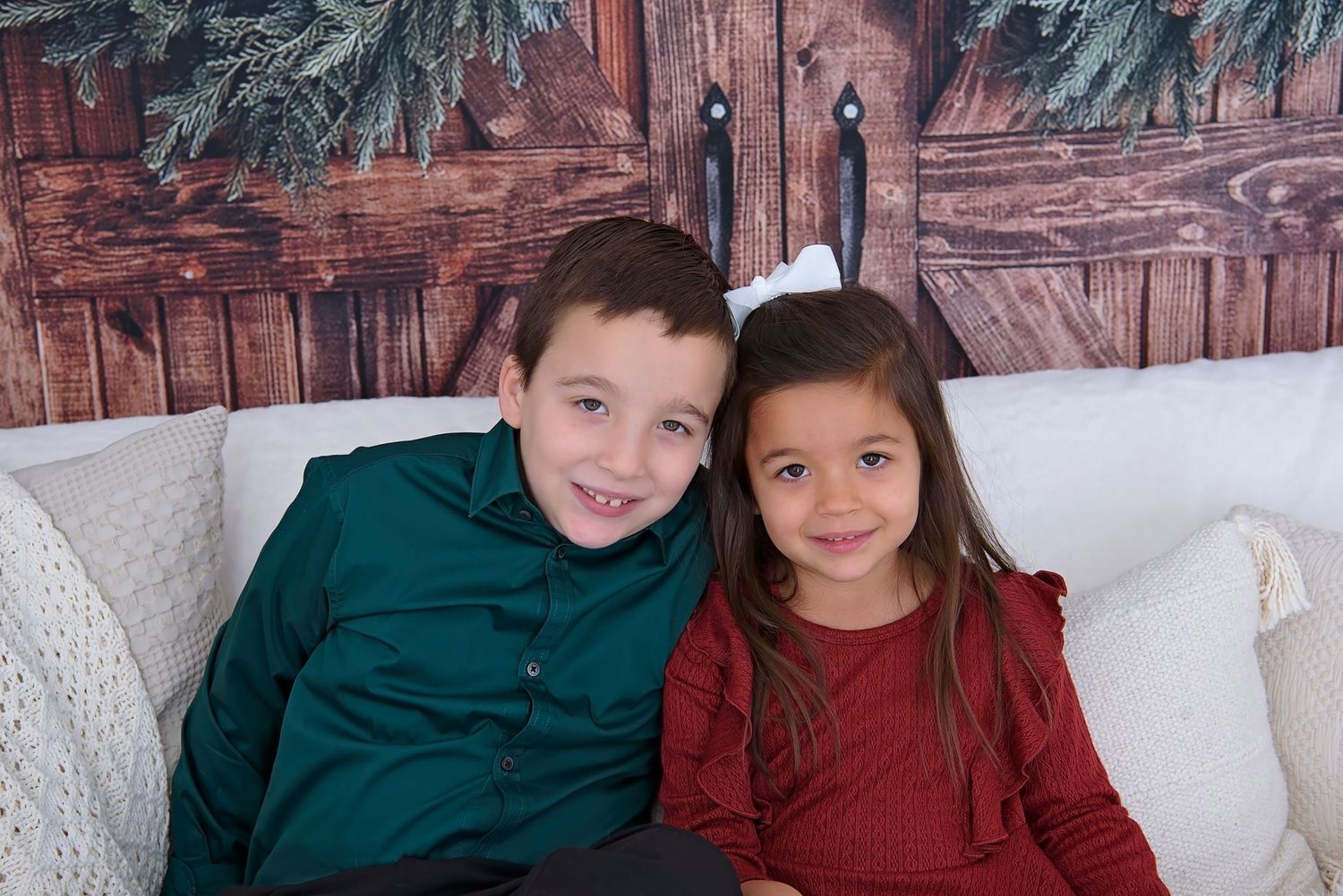 Children in coordinating burgundy and green holiday outfits pose together on a white couch.