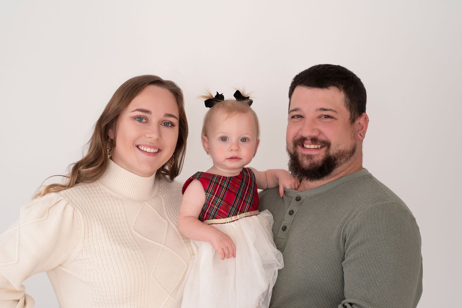 A family in matching cream sweaters poses together for a casual indoor portrait session.