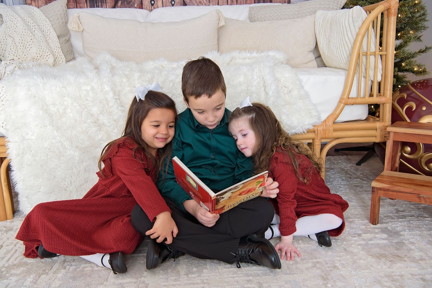 Children sitting together on a white couch with holiday decor and red accents in the background.