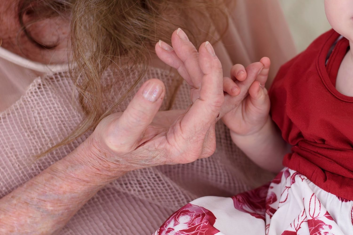 Two sets of hands reaching towards each other against a soft pink and red background.