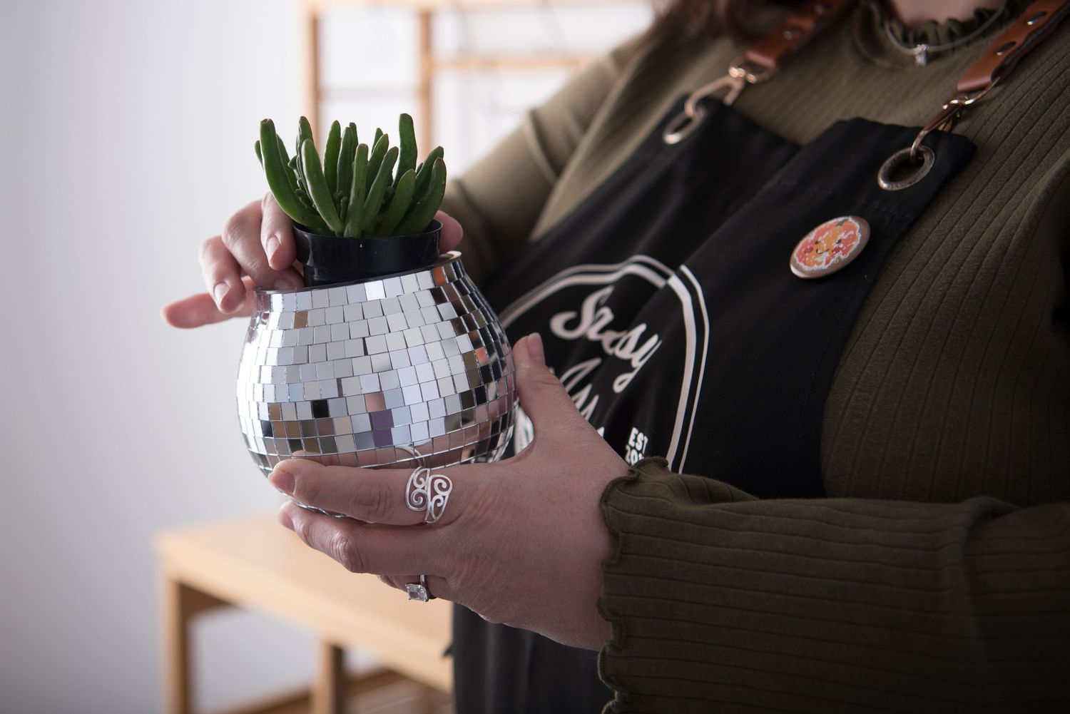 Hands holding and planting small green succulent plants in white ceramic pots on a wooden surface.