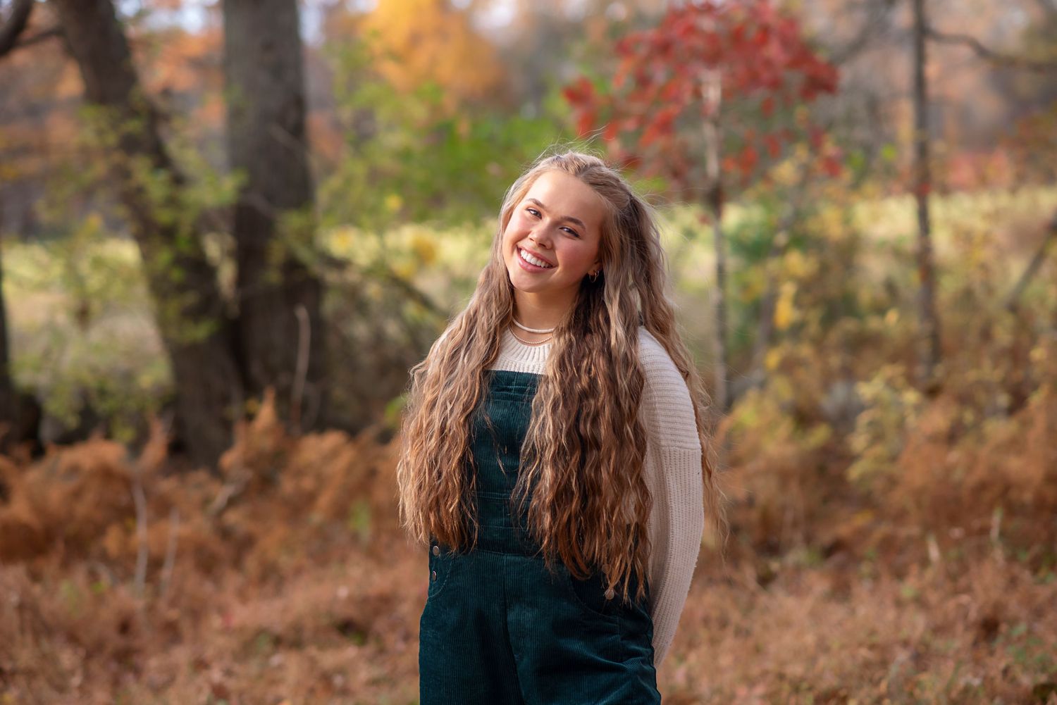 A person in a green velvet dress poses outdoors against a warm autumn background with fall foliage. Rhode Island Photographer