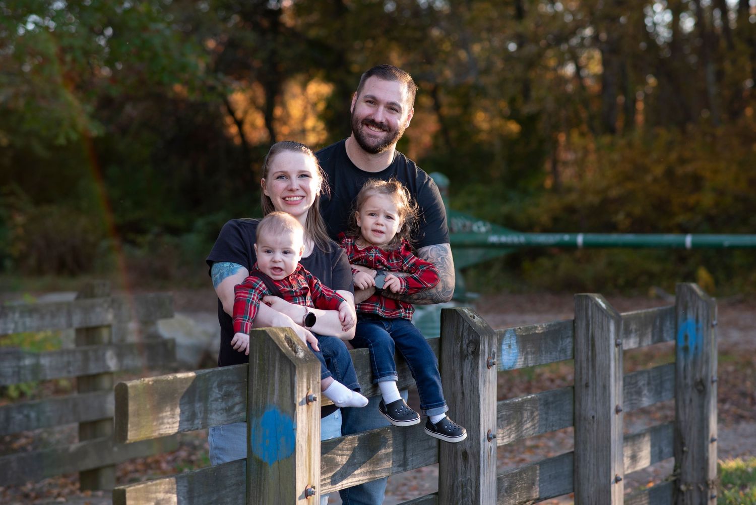 Family enjoying a sunny autumn day outdoors on a wooden fence with fall foliage in the background.
