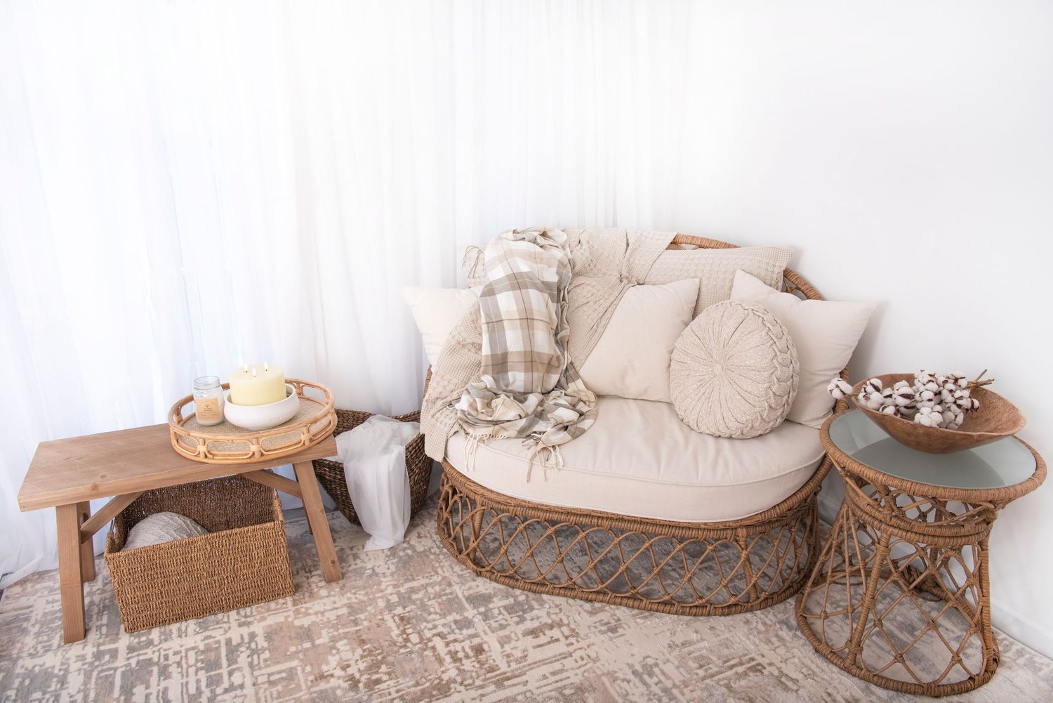 Cozy living room corner with rattan loveseat, wooden side tables, plush pillows and neutral decor on textured rug. Rhode Island Photographer