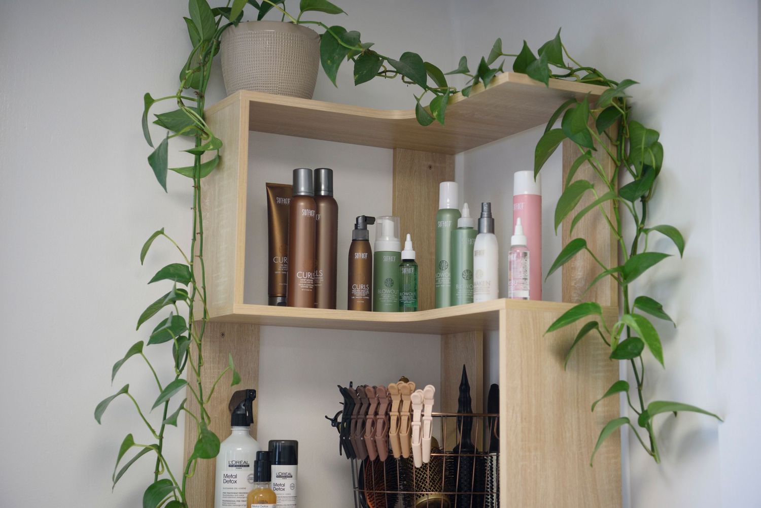 Natural wood bathroom shelf decorated with climbing vine plants and displaying various beauty and hair care products.