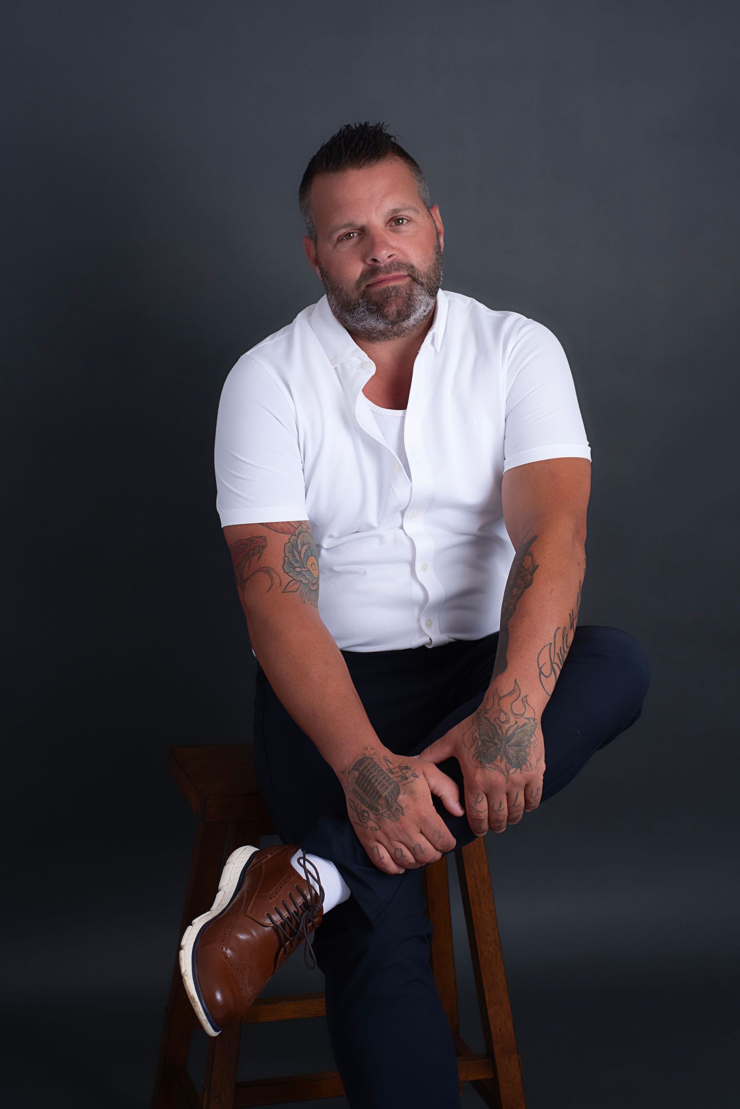 A series of dramatic studio portraits showing someone in a white t-shirt and dark pants seated on a wooden stool.