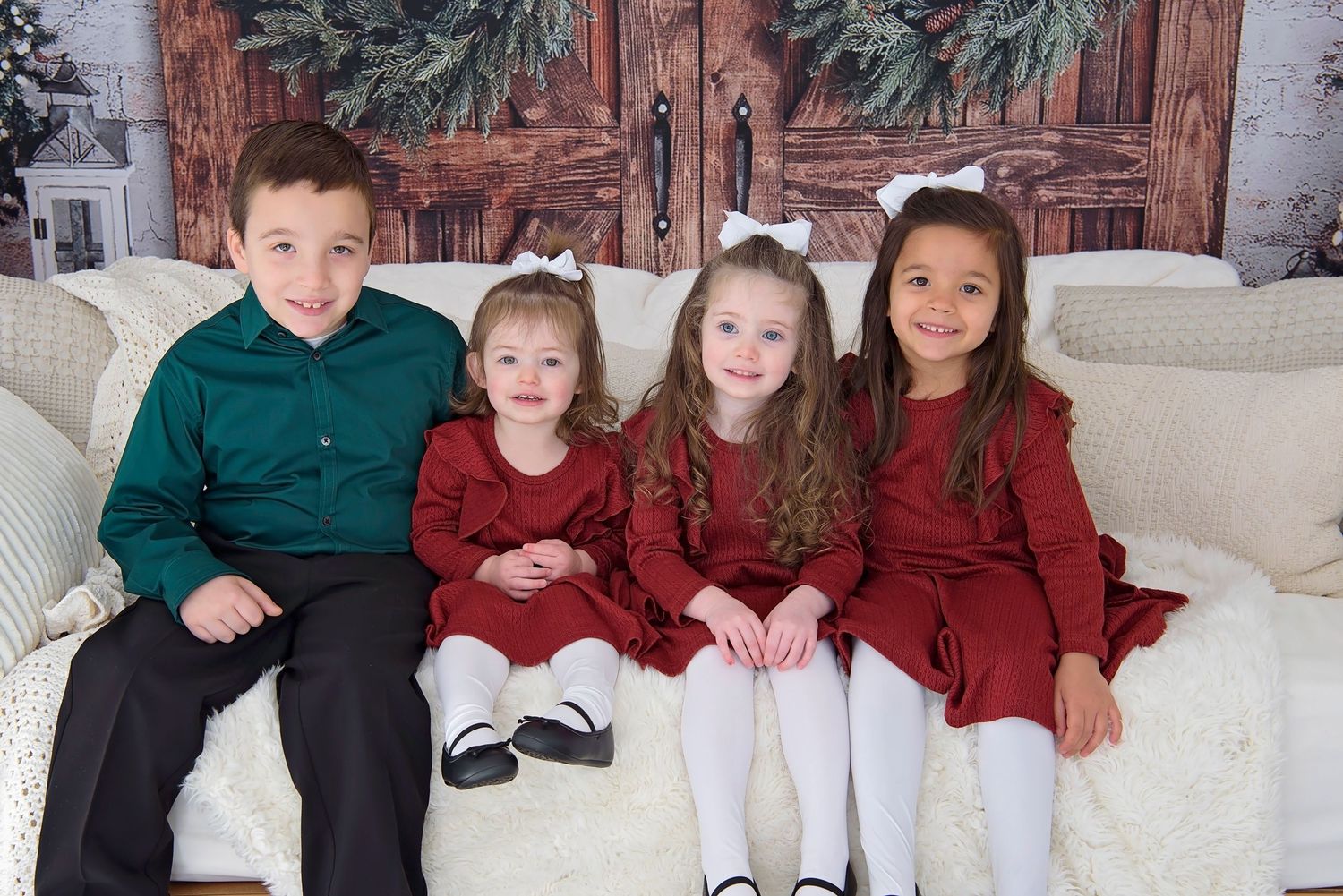 A group wearing coordinated red and green holiday outfits sits together on a white couch for a festive family photo.