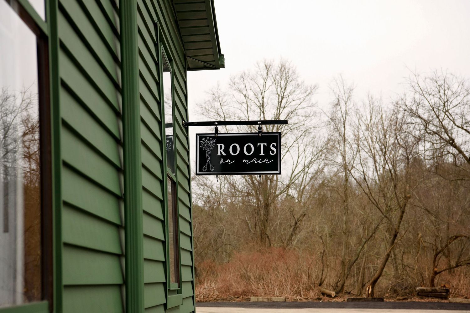 A black and white 'Roots' sign hangs on a green building exterior with bare trees in the background.