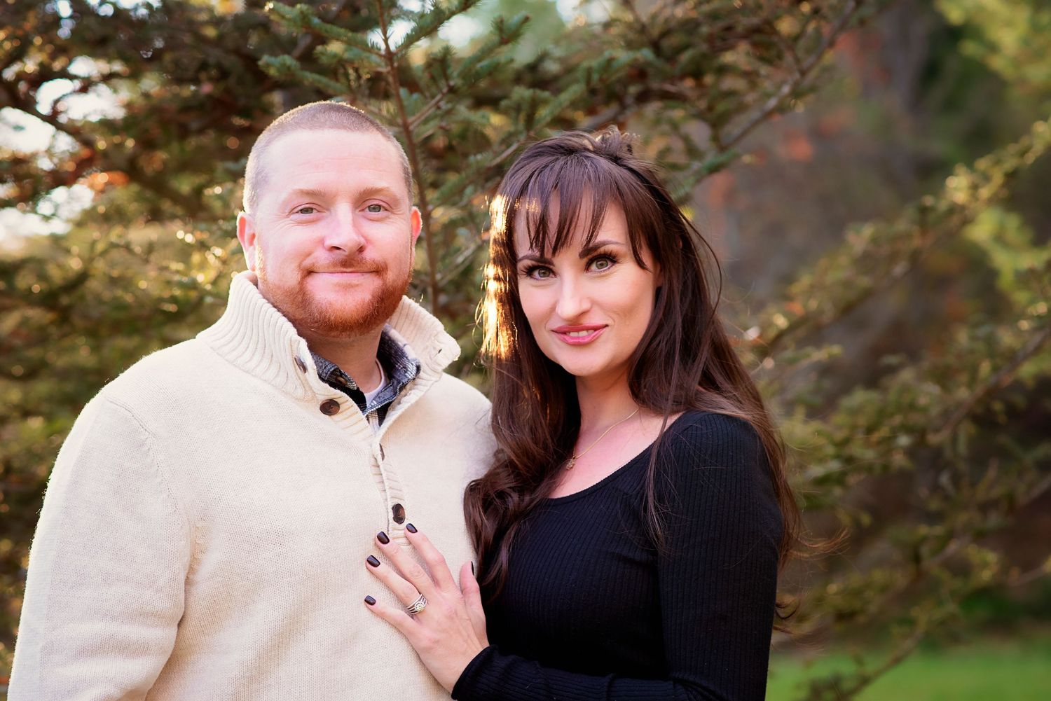 A couple sharing intimate moments together in a garden setting with evergreen trees in the background.