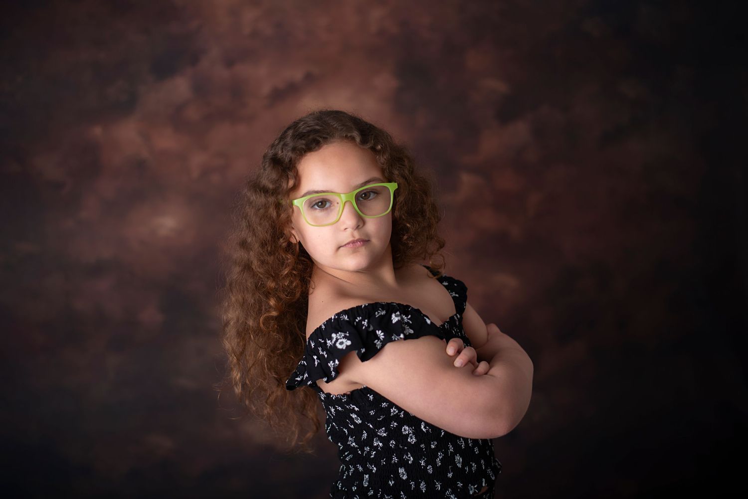 Studio portrait of someone wearing a black and white polka dot dress against a dark rustic brown background.